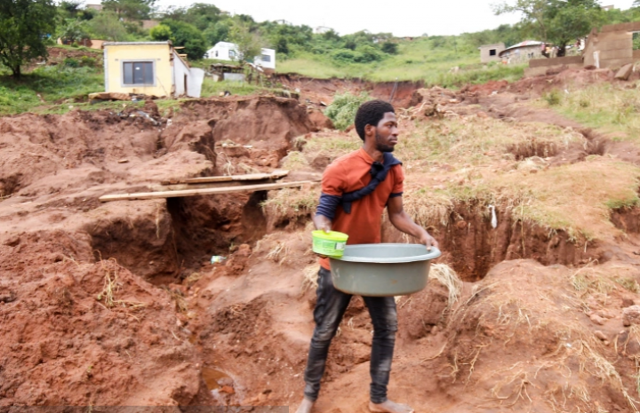 Mthandi Sibiya mengumpulkan air di dekat sisa-sisa rumahnya yang runtuh saat dia tidur karena banjir di Mzinyathi dekat Durban, Afrika Selatan, pada 17 April 2022 [Rogan Ward/ Reuters]