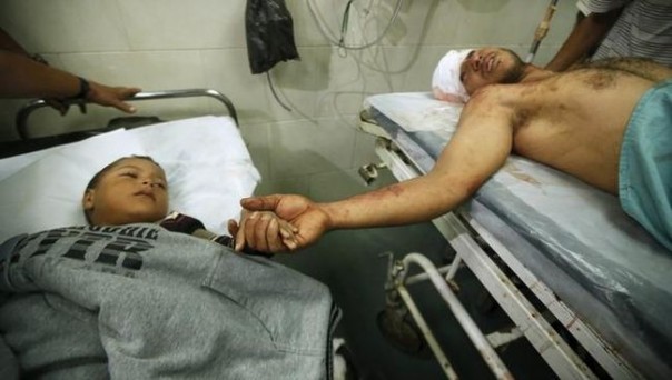 Seorang pria dewasa Palestina memegang tangan seorang bocah Palestina yang dirawat di sampingnya, di salah satu rumah sakit di Gaza. Saat ini, kondisi rumah sakit di kawasan itu semakin memprihatikan. Foto: int 