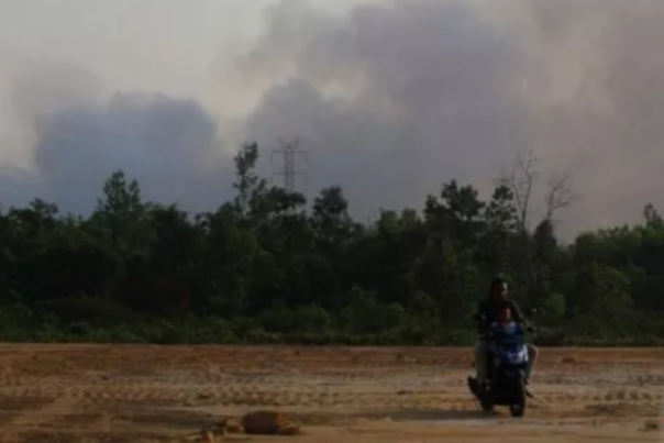 Seorang warga Kota Dumai mengendari motor dengan latar belakang lahan yang terbakar. Foto: int 