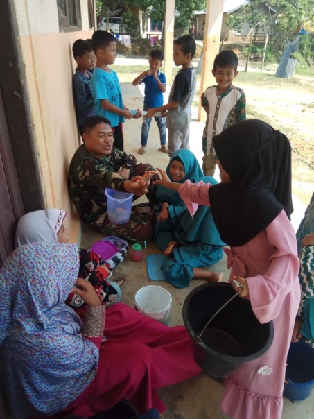 anggota satgas TMMD ke 105 Serma Sunarno Dari Batalyon Arhanud 13/BS Pekanbaru saat bersama Aura dan Aurel di Desa Balung
