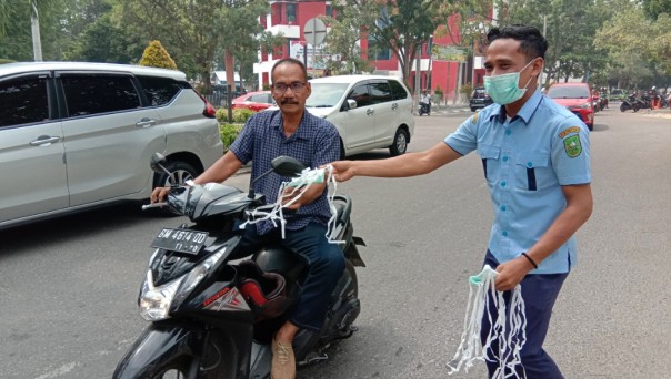 Petugas Dinas Kesehatan Provinsi Riau memberikan sebuah masker kepada pengendara