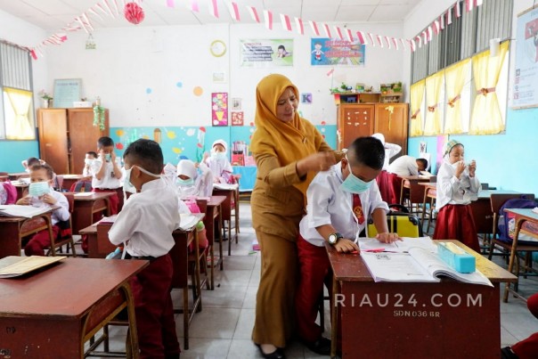 Seorang guru di salah satu sekolah di Pekanbaru memakaikan masker kepada muridnya dikarenakan kabut asap yang masih menyelimuti Kota Bertuah