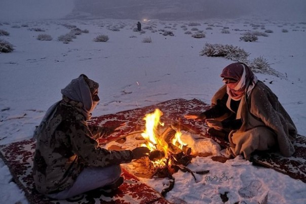 Dua pria di Tabuk, Arab Saudi, duduk menghangatkan diri di dekat api dengan salju di sekitar mereka. Foto/Gulf News/Twitter