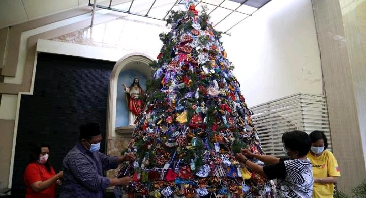 Ustaz Nur Kholis Saleh membantu umat Kristiani merangkai pohon Natal dari masker di Gereja Katolik Kristus Raja, Surabaya, Jawa Timur, Jumat (18/12/2020). (net)