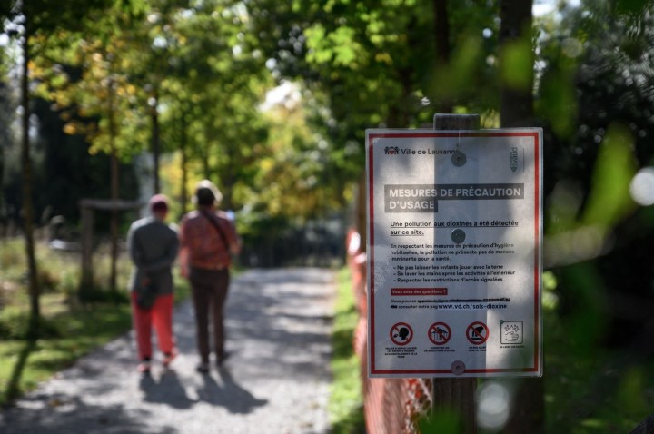 Papan peringatan di sebelah taman bermain la Sallaz yang tercemar dioksin dikelilingi oleh pagar oranye di Lausanne, Swiss, 15 Oktober 2021. (AFP Photo)
