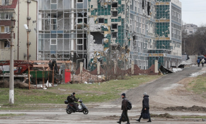 Orang-orang melewati gedung yang rusak selama invasi Rusia ke kota pelabuhan selatan Mariupol pada 4 April [Alexander Ermochenko/Reuters]