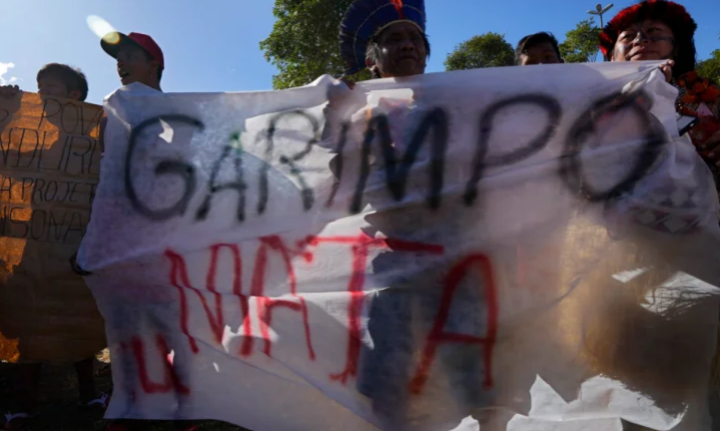 Masyarakat Adat Munduruku membawa spanduk dengan teks tertulis dalam bahasa Portugis bertuliskan 'Mining Kills', selama pawai untuk demarkasi tanah Adat pada 6 April di Brasilia [Eraldo Peres/AP Photo]