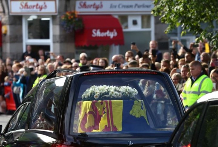 Orang-orang berbaris di jalan saat mobil jenazah yang membawa peti mati Ratu Elizabeth II melewati desa Ballater di Skotlandia [Hannah McKay/Reuters]