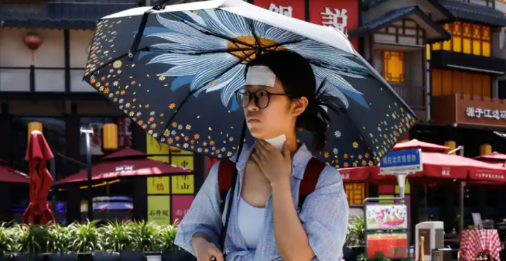 Seorang wanita berjalan dengan bercak dingin di dahi dan lehernya di tengah peringatan merah untuk gelombang panas di China /Reuters