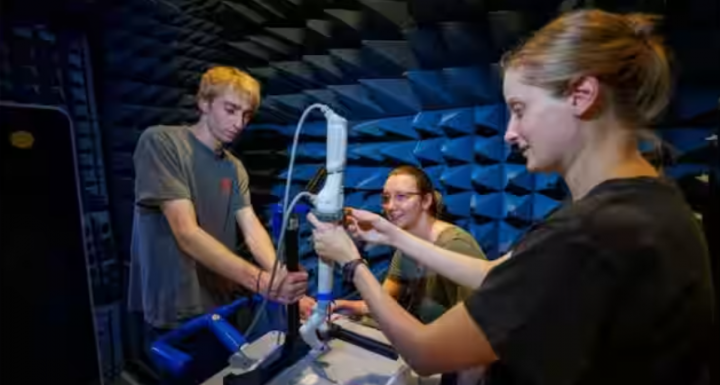 Dalam gambar ini milik Virtual Incision (LR) Sean Crimmins, senior di bidang teknik; Erika Smith, mahasiswa Universitas Nebraska Lincoln (UNL); dan Rachael Wagner, seorang mahasiswa pascasarjana UNL, menyesuaikan lengan robot pada dudukan di ruang untuk pengujian Kompatibilitas Elektromagnetik (EMC)