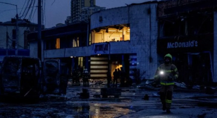 Seorang petugas pemadam kebakaran menyinari senter di dekat bangkai mobil yang terbakar, stasiun metro yang rusak, dan McDonald's, menyusul serangan roket di Kyiv, pada 18 Januari 2025, di tengah invasi Rusia ke Ukraina /AFP