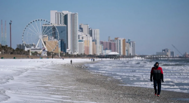 Seorang pria berjalan di sepanjang pantai yang tertutup salju pada 22 Januari 2025 di Myrtle Beach, Carolina Selatan /AFP