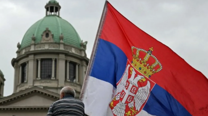 Seorang pengunjuk rasa yang memegang bendera nasional, duduk di atap traktor saat dia dan yang lainnya berkumpul di depan gedung Majelis Nasional selama salah satu protes terbesar sejak gerakan anti-korupsi, di Beograd pada 15 Maret 2025 /AFP